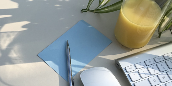 Blue index card and silver pen, mouse and keyboard and a fresh squeezed orange juice